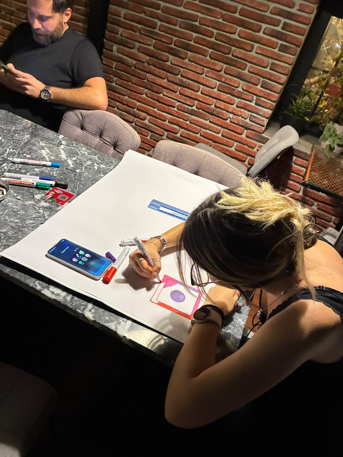 Bir katılımcı masadaki büyük kâğıda Instagram logosu çiziyor.